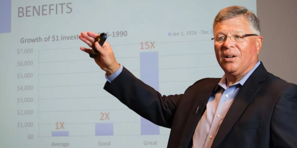 Bobby Albert speaking to an audience, gesturing toward a slide charting the growth of $1 invested from 1926 to 1990.