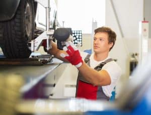 Young serviceman checking wheel alignment in a car workshop