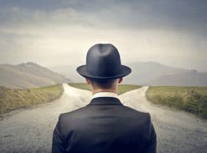 Man looking at fork in the road asking himself, what is more important, managing or leading?
